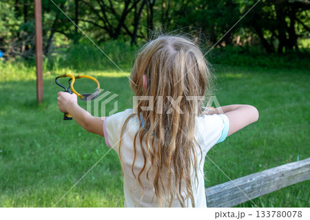 Child practices aiming with a slingshot in a green backyard during a sunny afternoon 133780078