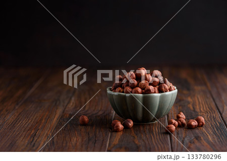 Hazelnuts in a bowl on a dark wooden background. Front view 133780296