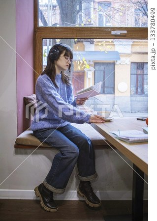 Young woman reading a book in a cozy cafe with a cup of cocoa. Young woman reading a book in a cozy cafe with a cup of cocoa. 133780499