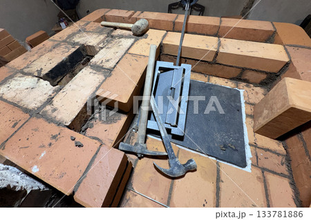 Installation of the cooking plate for a heating stove. Brickwork during the construction of a heating stove. Tools are laid out around. 133781886