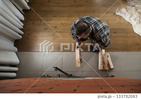 Caucasian adult man holding wooden log near open stove door while heating bright indoor room with rustic brick construction. Winter Firewood Routine Preparing and Lighting a Wood Stove Caucasian adult man holding wooden log near open stove door while heating bright indoor room with rustic brick construction. Winter Firewood Routine Preparing and Lighting a Wood Stove 133782083