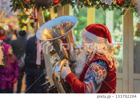 Santa Claus playing tuba at outdoor Christmas market with festive decorations and falling snow. Concept of holiday celebration, music and joyful spirit of Christmas tradition Santa Claus playing tuba at outdoor Christmas market with festive decorations and falling snow. Concept of holiday celebration, music and joyful spirit of Christmas tradition 133782204