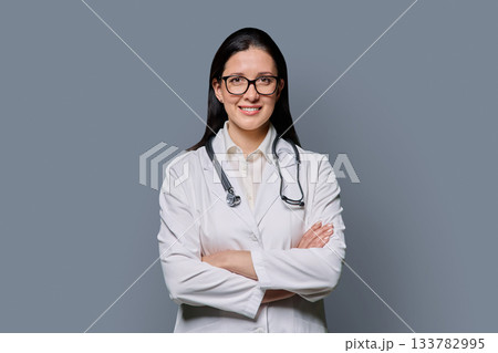 Portrait of smiling female doctor in white lab coat with stethoscope on gray background Portrait of smiling female doctor in white lab coat with stethoscope on gray background 133782995
