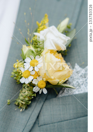 Floral boutonniere featuring yellow and white blooms, including roses and daisies, on a textured suit lapel. Perfect for weddings and formal events to add a touch of elegance. Floral boutonniere featuring yellow and white blooms, including roses and daisies, on a textured suit lapel. Perfect for weddings and formal events to add a touch of elegance. 133783316