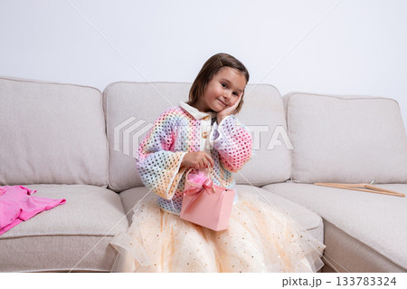 Caucasian young girl with gift on sofa in colorful sweater and tulle skirt Caucasian young girl with gift on sofa in colorful sweater and tulle skirt 133783324