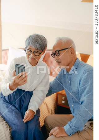 ホテルでスマホを見ながら会話するシニア夫婦 ホテルでスマホを見ながら会話するシニア夫婦 133783410
