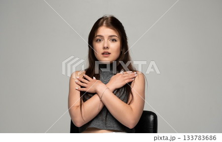 Surprised young woman with crossed arms on chest standing in studio against light grey background 133783686
