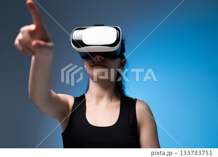 Woman interacting with virtual interface using VR headset and extended hand in clean futuristic blue studio Woman interacting with virtual interface using VR headset and extended hand in clean futuristic blue studio 133783751