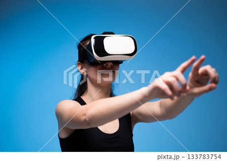 Woman wearing VR headset exploring digital space with expressive hand gestures in virtual environment Woman wearing VR headset exploring digital space with expressive hand gestures in virtual environment 133783754