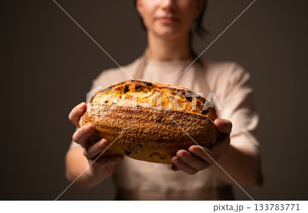Baker holding seeded artisan bread loaf with golden baked crust and textured surface in warm soft lighting 133783771