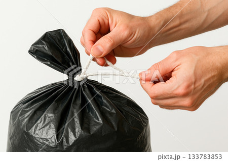 Tying a rope handle on a black garbage bag. Tying a rope handle on a black garbage bag. 133783853