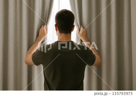 A man opens the curtains, letting in the light. A man opens the curtains, letting in the light. 133783973