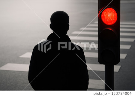 The silhouette of a man is waiting at a traffic light with a red signal. 133784004