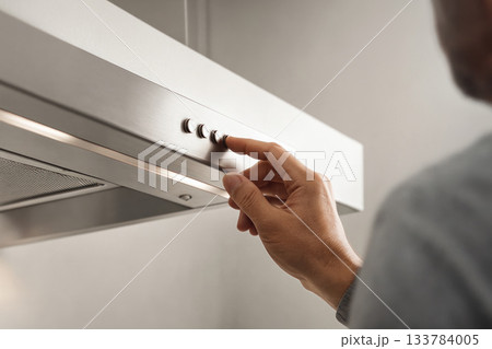 The man turns on the kitchen hood by pressing a button. 133784005