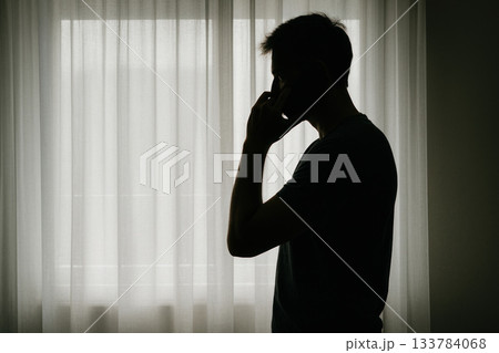 Silhouette of a man at the window talking on the phone. Space for text. 133784068