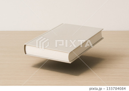 A closed book hovering in the air above the table. Space for text. A closed book hovering in the air above the table. Space for text. 133784084