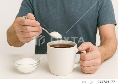 A person adds sugar to a mug of tea. A person adds sugar to a mug of tea. 133784177