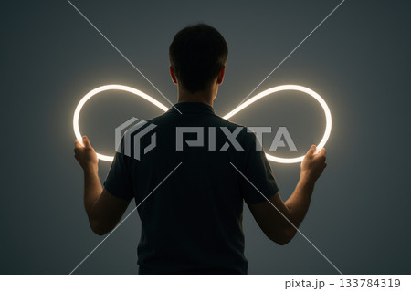 A person holds a luminous loop in the shape of an infinity symbol. 133784319