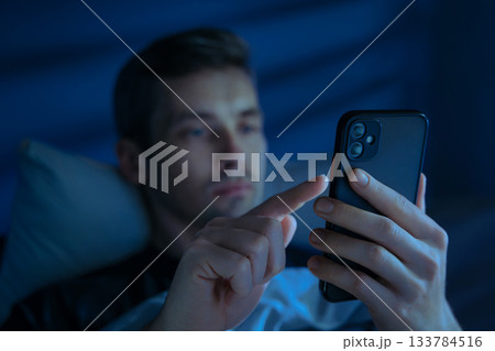 Man a dark bedroom, holding mobile phone and browsing social media at night Man a dark bedroom, holding mobile phone and browsing social media at night 133784516