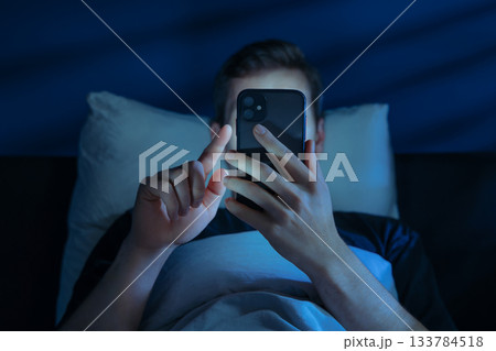 Man holds his smartphone close to face while brousing social media at night Man holds his smartphone close to face while brousing social media at night 133784518