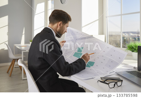 Businessman analyzing cadastral map while sitting at desk in office 133785598
