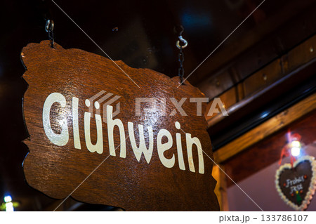 Rustic wooden sign Gluehwein in bright lettering hangs above a festive stall, inviting visitors to enjoy traditional mulled wine at a german christmas market 133786107