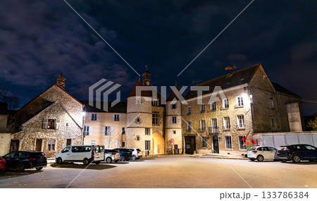 Night view of the historic town hall of Tournan-en-Brie in Paris Region of France. The stone town hall and surrounding buildings are illuminated under a cloudy dark sky 133786384