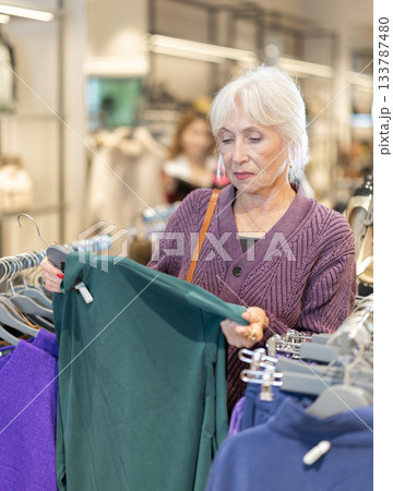 Positive mature woman choosing pullover in clothing store 133787480