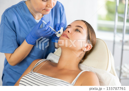 Adult woman cosmetologist makes injection in lips of patient Adult woman cosmetologist makes injection in lips of patient 133787761