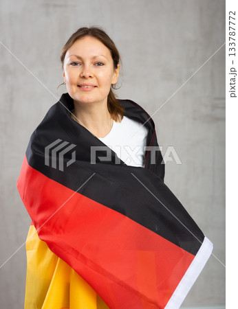 Happy young woman holding flag of Germany against unicoloured background 133787772