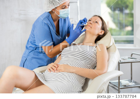 Young female cosmetologist makes injection in lips of patient Young female cosmetologist makes injection in lips of patient 133787784