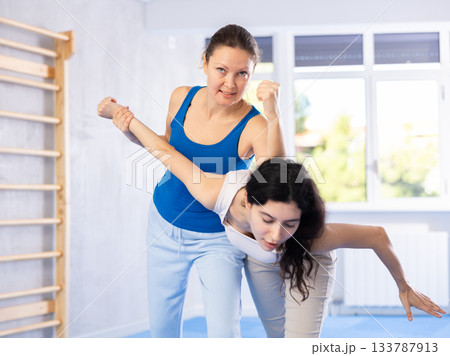 Woman is practicing self defence moves in pair with her female trainer at gym 133787913