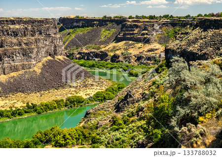 Green Snake River winds through rugged basalt cliffs of Snake River Canyon in Twin Falls, Idaho. Scenic landscape highlights dramatic geology of American West with contrast between arid canyon walls 133788032