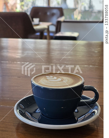 beautifully crafted coffee cup with latte art sits on wooden table, creating cozy atmosphere in cafe. background features blurred chairs, enhancing inviting vibe 133788058