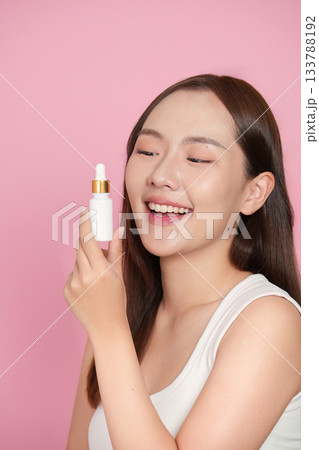 Skincare Routine. Young woman applying serum with a dropper, smiling brightly. Skincare Routine. Young woman applying serum with a dropper, smiling brightly. 133788192