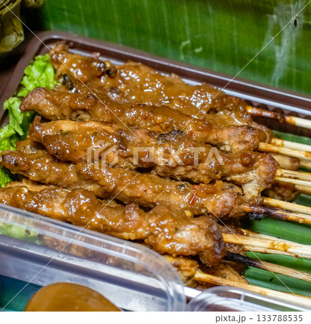 Close-up photo of chicken satay (sate ayam) on bamboo skewers, coated in peanut sauce and served on banana leaf 133788535
