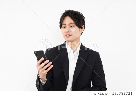 白い背景でスマホを操作する若いビジネスマン 白い背景でスマホを操作する若いビジネスマン 133788721