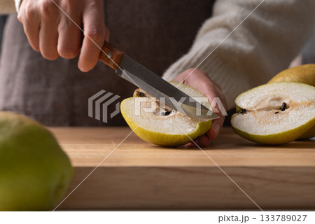 Hand holding kitchen knife and cutting pear on wooden board 133789027