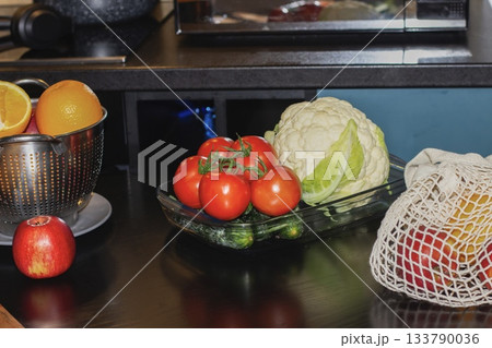 Fresh cucumbers and tomatoes laid out on a plate on the kitchen table, with fresh fruits and vegetables in the background. Useful ingredients for making salad at home. Fresh cucumbers and tomatoes laid out on a plate on the kitchen table, with fresh fruits and vegetables in the background. Useful ingredients for making salad at home. 133790036