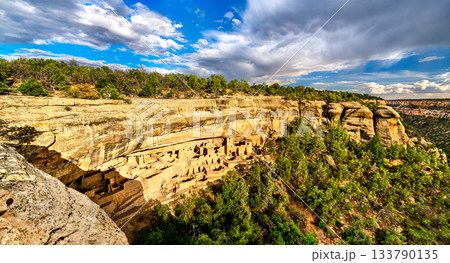 Cliff Palace ruins sit in alcove of sandstone canyon in Mesa Verde National Park, Colorado. Ancient Ancestral Puebloan dwellings feature stone walls and kivas under cloudy sky 133790135