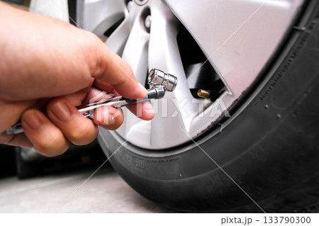 Hand using a tire pressure gauge on a car valve stem Hand using a tire pressure gauge on a car valve stem 133790300