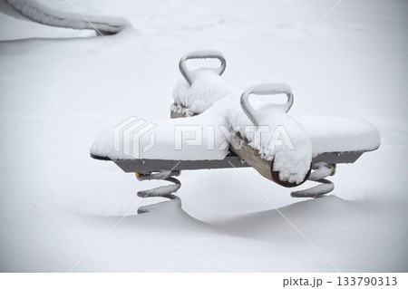Snow-covered playground equipment in winter, a seesaw covered in snow 133790313