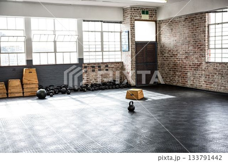 Single black kettlebell is sitting on rubber floor inside brick gym under grid windows, plyo boxes Single black kettlebell is sitting on rubber floor inside brick gym under grid windows, plyo boxes 133791442