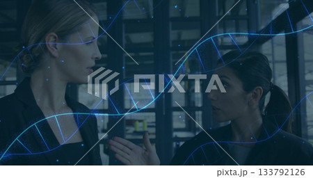 Speaking two businesswomen discussing biotech data in office space, with DNA helix overlay 133792126
