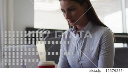 Typing woman in blue shirt working at office desk, with silver laptop, red-sleeved coffee cup 133792254