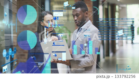 Reviewing consultants in formal attire analyzing laptop at office corridor, with floating charts 133792256