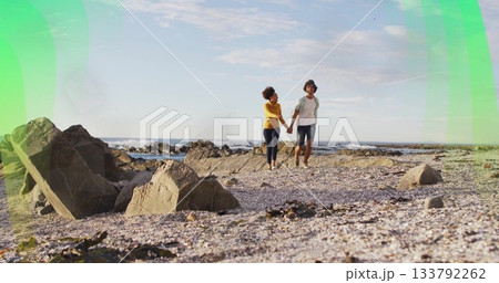Walking man and woman holding hands on rocky shoreline, with pebbles shells ocean waves 133792262