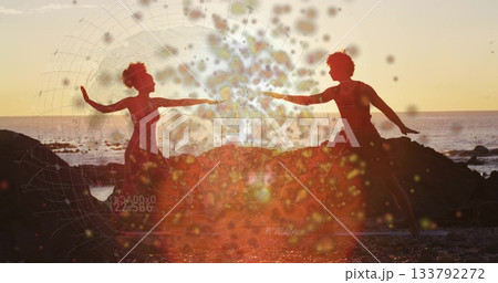 Dance duo performing mirrored yoga pose on rocky beach at sunset, with yoga mats, bokeh overlay 133792272