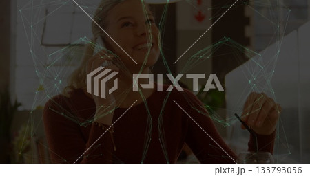 Talking woman in sweater holding phone, lifting glass with straw at cafe table with network overlay Talking woman in sweater holding phone, lifting glass with straw at cafe table with network overlay 133793056