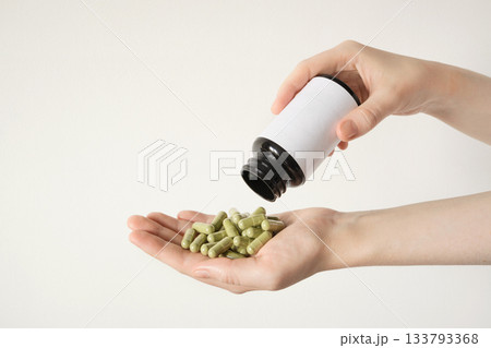 Female hand pouring green encapsulated supplements from generic bottle, highlighting health and wellness 133793368